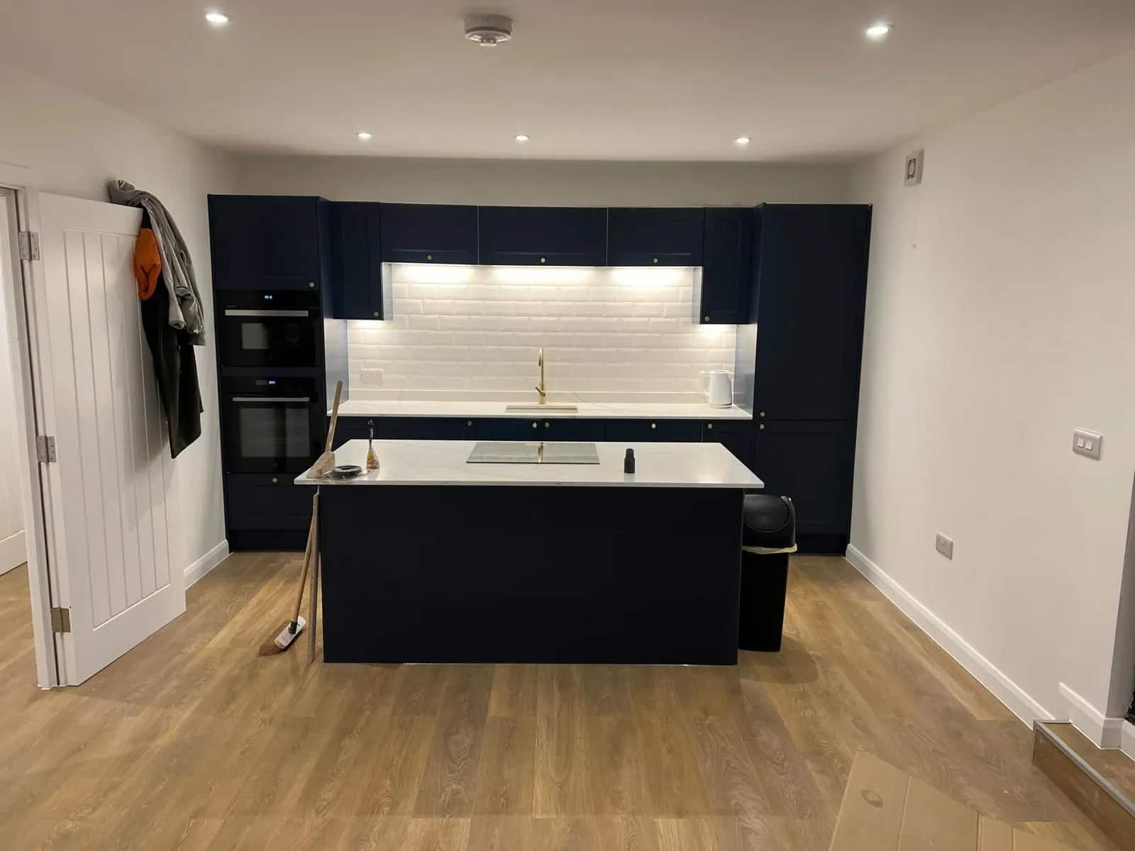 Navy shaker kitchen with a marble-effect island, brass tap and white metro tile splashback