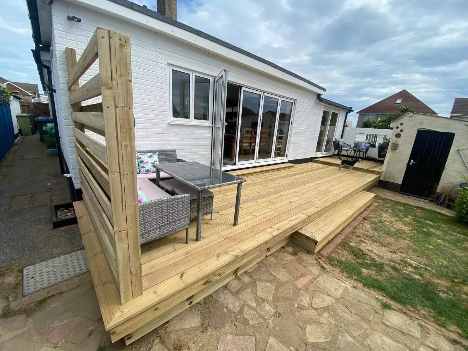 Softwood garden deck with a horizontal slatted screen beside a white rendered bungalow
