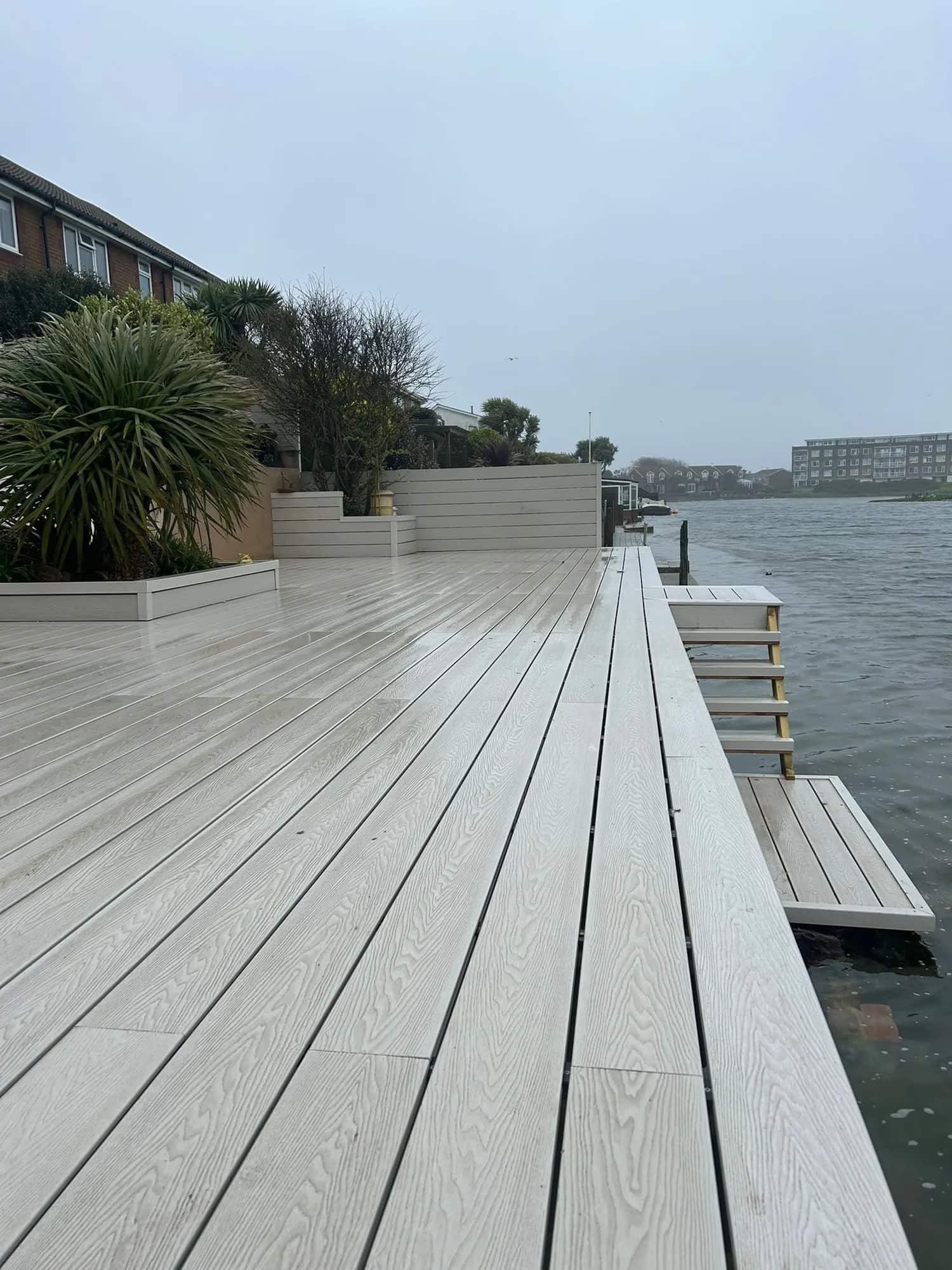 Grey composite decking running along an estuary edge with a slatted privacy screen and planters