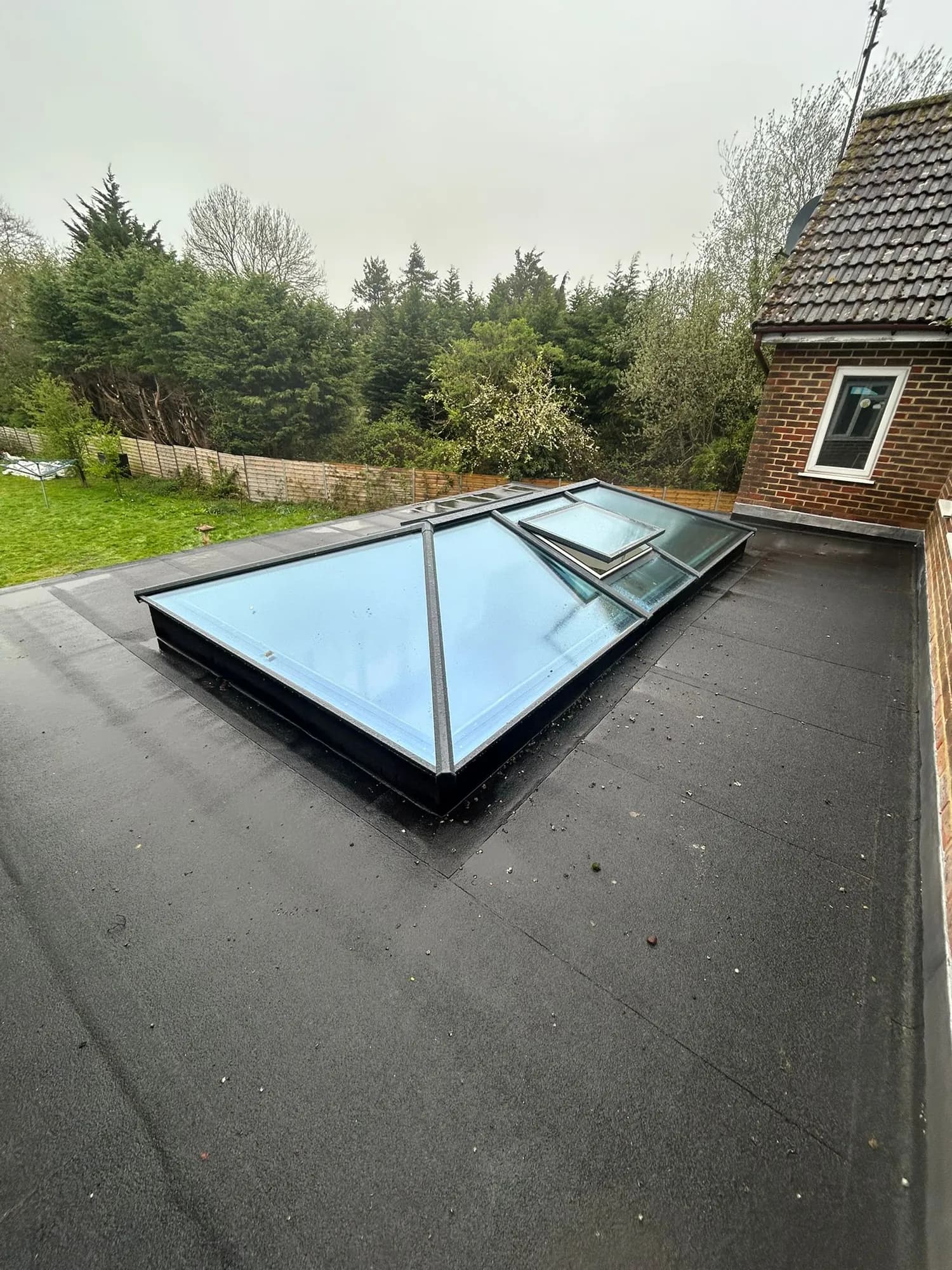 Glazed roof lantern set into a new felted flat roof behind a brick house